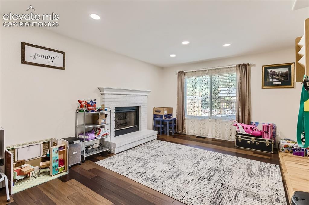 Image 15 of 49: Recessed lighting, wood-finish flooring, brick fireplace with mantel, and a