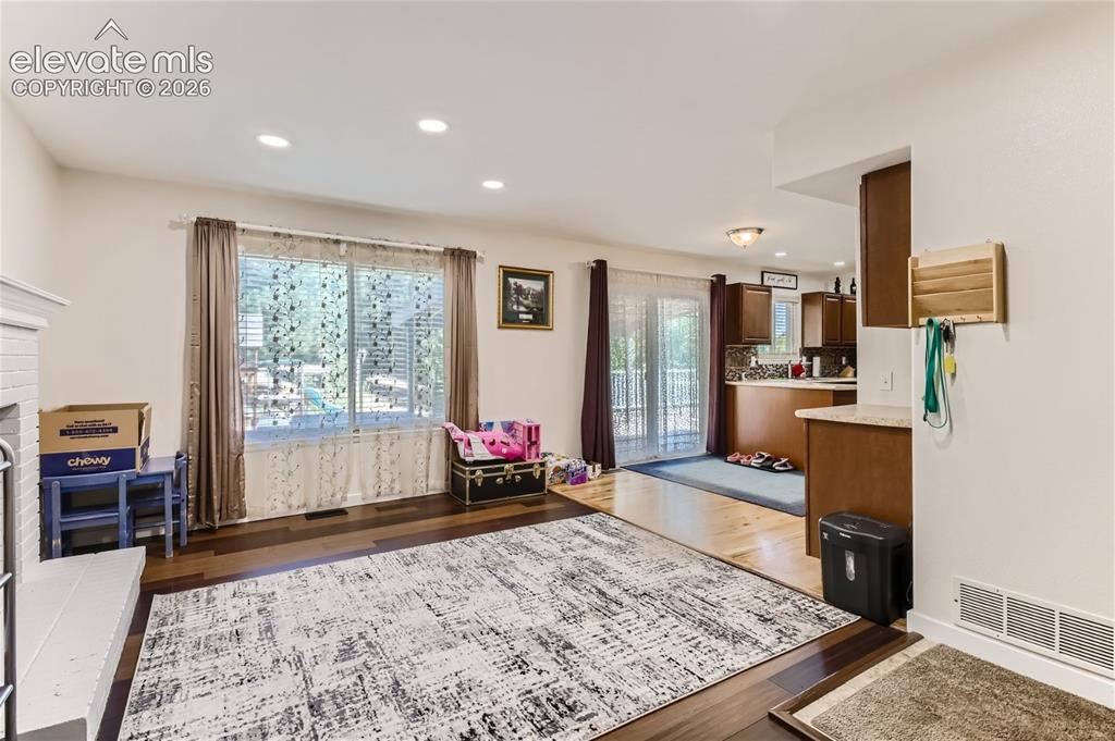 Image 16 of 49: Recessed lighting, wood-finish flooring, white brick fireplace, kitchen wit
