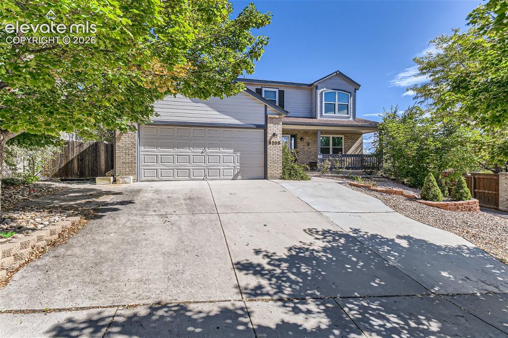 Image 2 of 49: Expansive concrete driveway, attached garage, brick facade with siding, cov