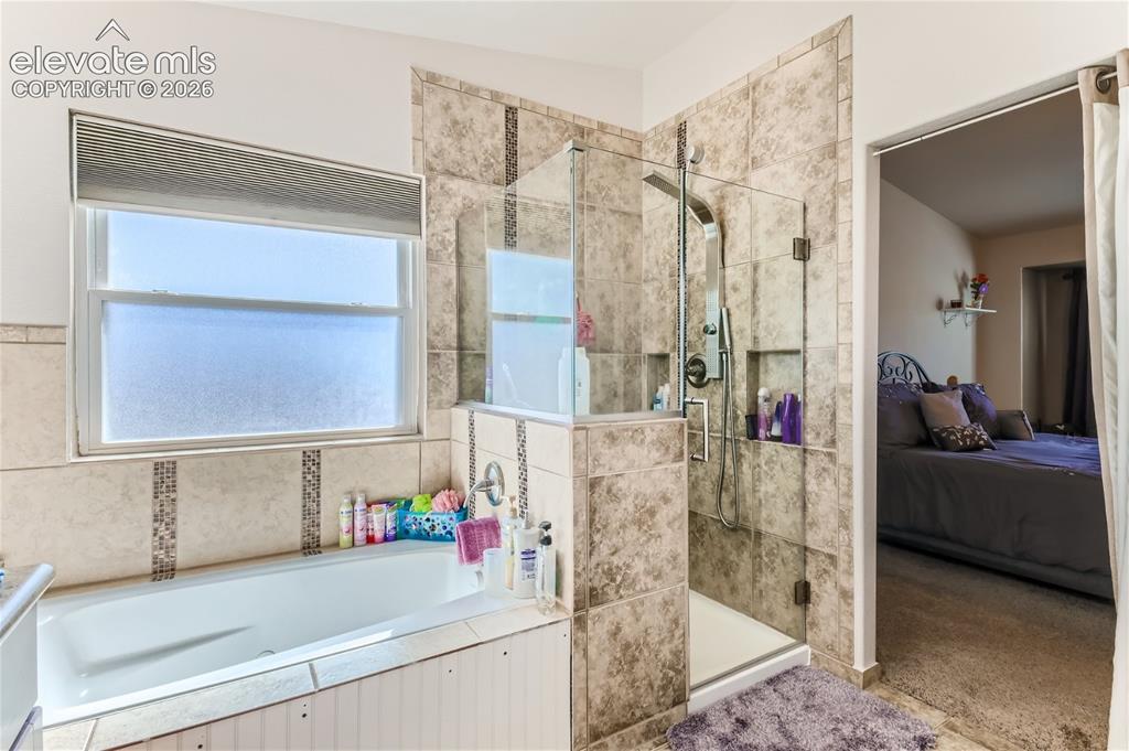 Image 22 of 49: Tiled shower enclosure with glass door, recessed shelving, and a rain showe