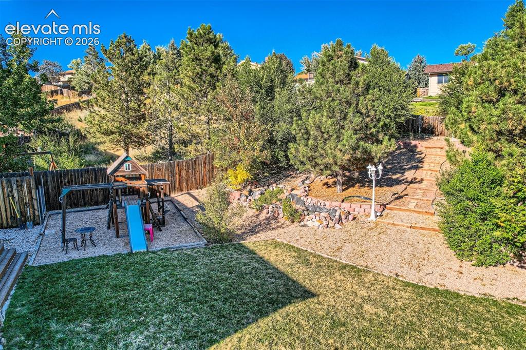 Image 49 of 49: Expansive rear yard featuring green lawn, a dedicated play area, and a tier