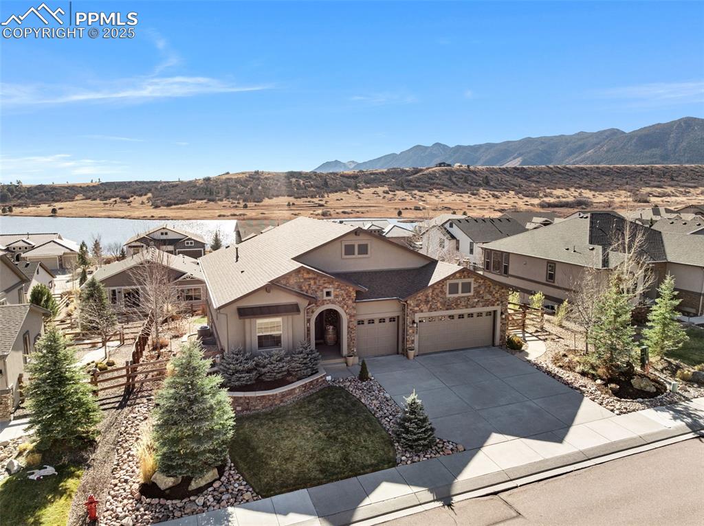 Caption: View of front of house with stucco and stone siding, concrete driveway, a lake and mountain view, an