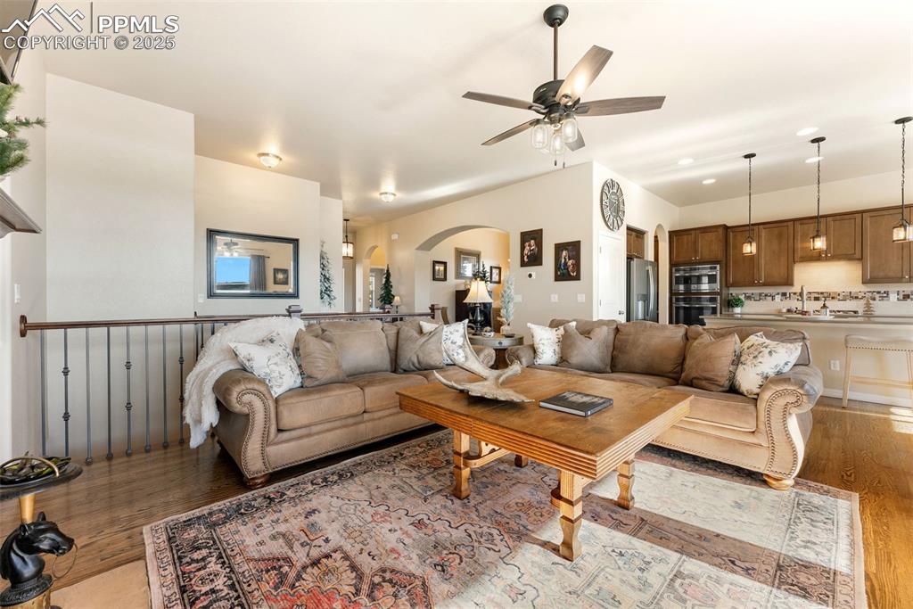 Image 18 of 50: Living room with arched walkways, hardwood floors, a ceiling fan, and reces