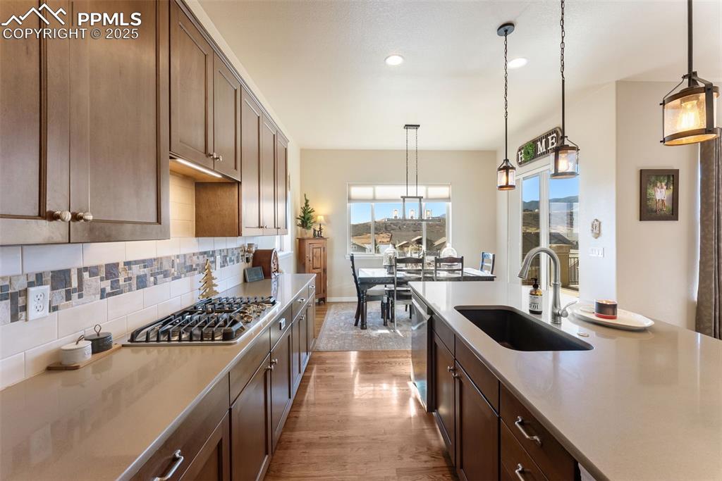 Image 6 of 50: Kitchen with backsplash, gas cooktop, decorative light fixtures, hardwood f