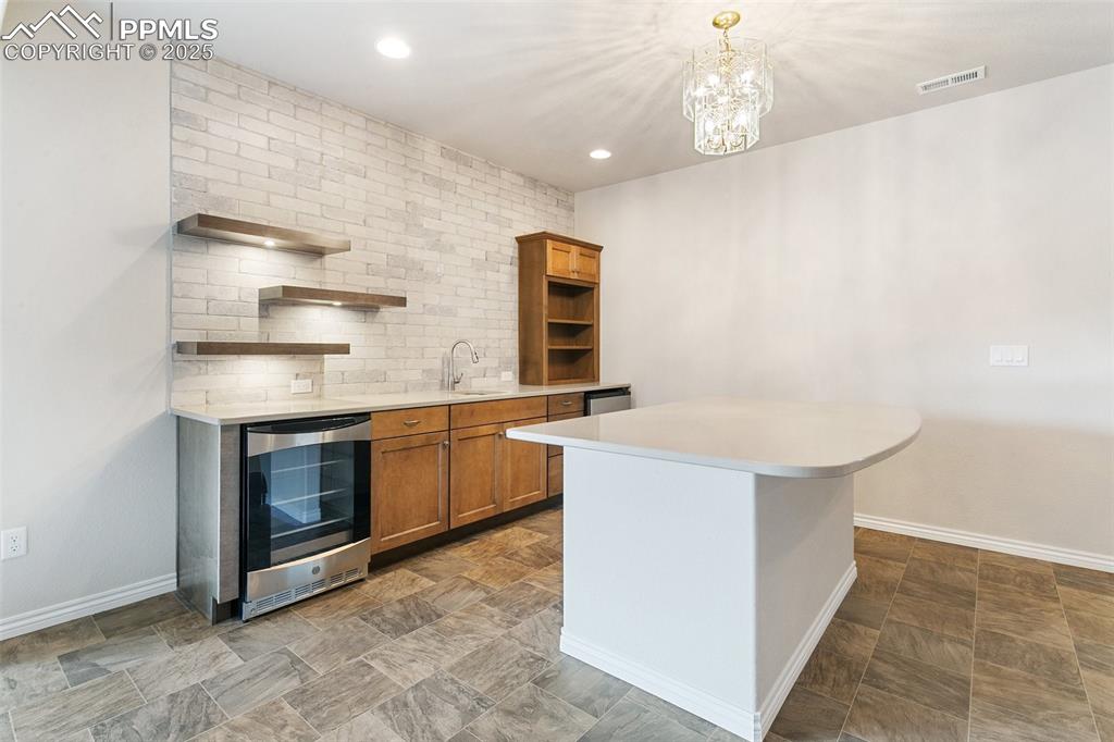 Image 25 of 41: Kitchen featuring beverage cooler, open shelves, brown cabinetry, light cou