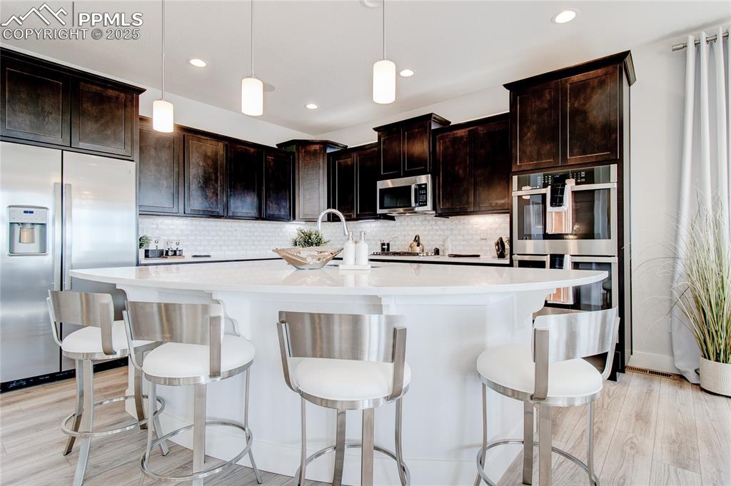 Image 5 of 30: Kitchen featuring stainless steel appliances, light countertops, backsplash