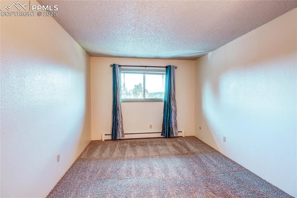 Image 16 of 20: Empty room with a baseboard heating unit, carpet, and a textured ceiling