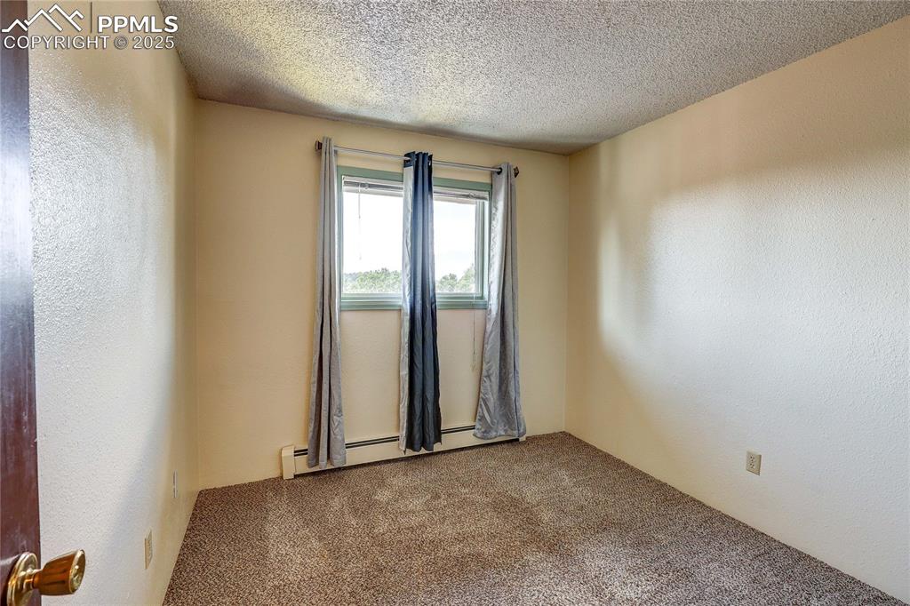 Image 18 of 20: Spare room featuring carpet floors, baseboard heating, a textured ceiling, 