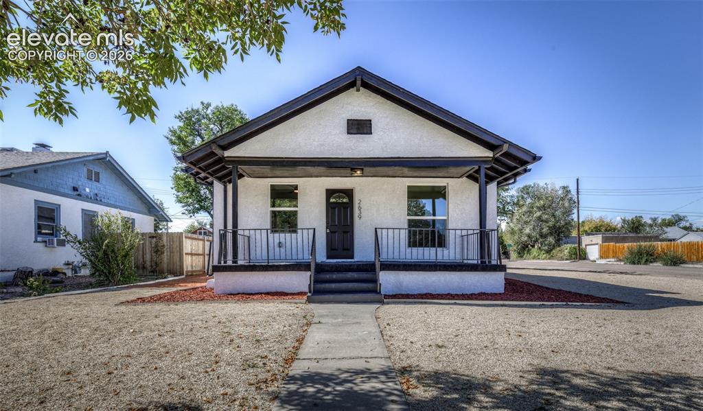 Caption: Stucco exterior featuring a covered front porch, dark-finished railings, a gabled roofline, and low-