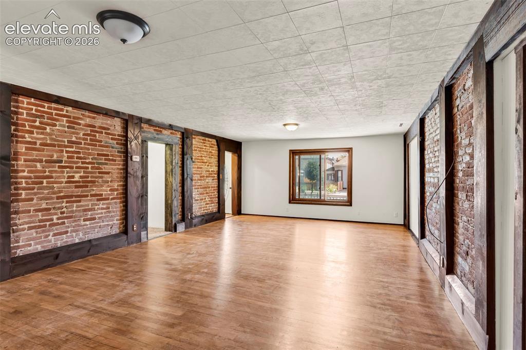 Image 10 of 29: Spacious room featuring exposed brick walls framed by dark wood beams, wood