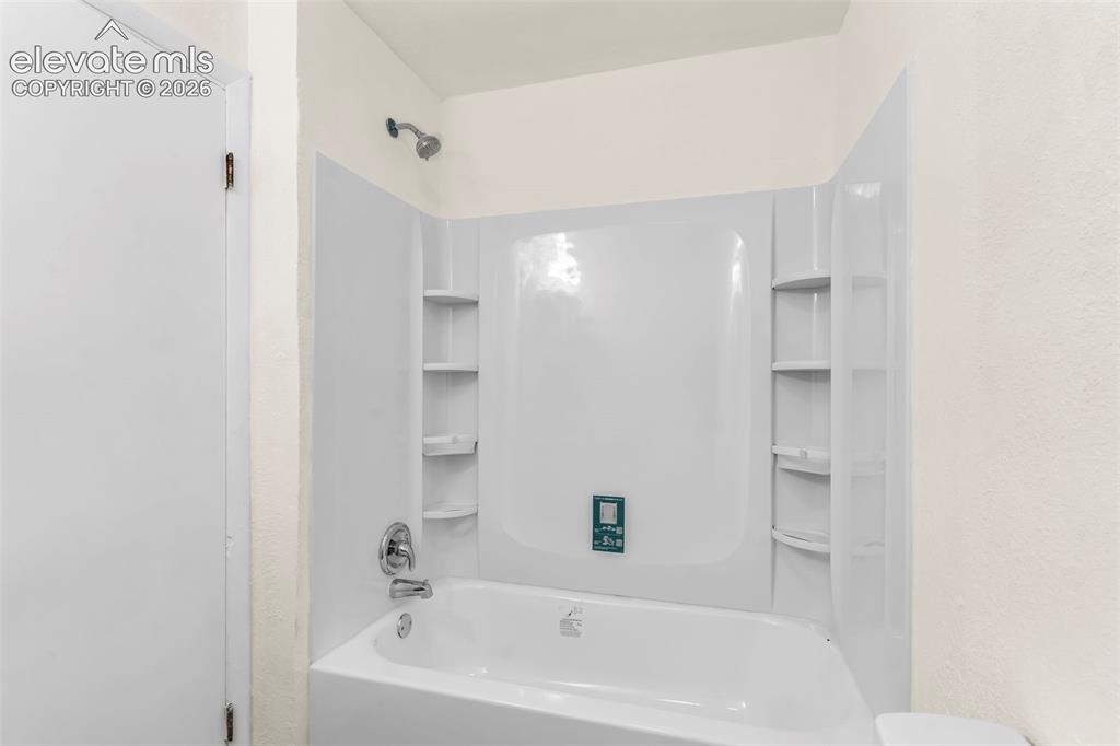 Image 18 of 29: White tub and shower combination with chrome fixtures and integrated shelvi