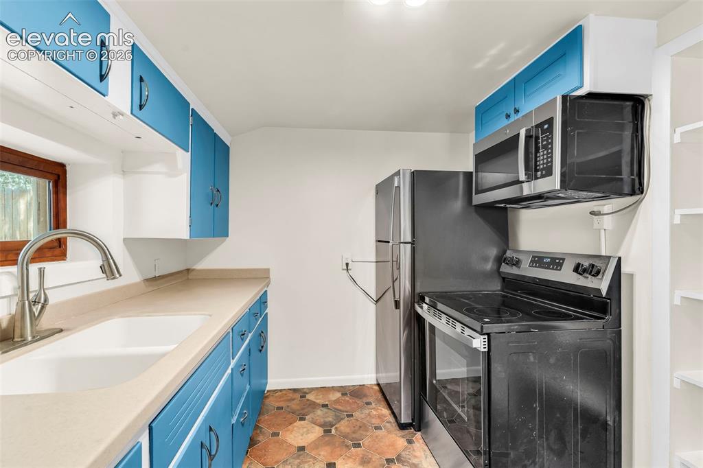 Image 23 of 29: Kitchen featuring bright blue cabinetry, a stainless steel sink with a goos