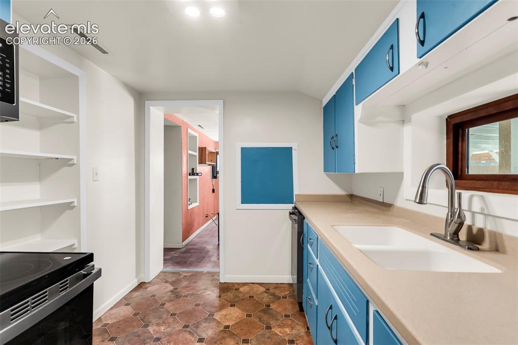 Image 24 of 29: Kitchen featuring light-toned countertops, a stainless steel sink with a hi