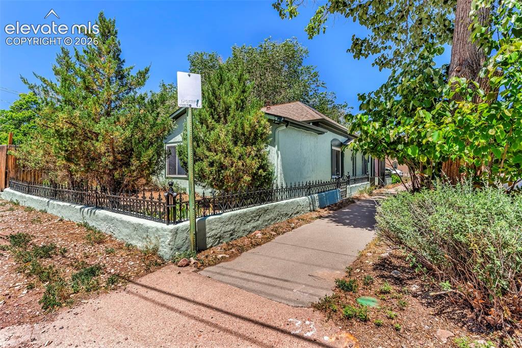 Image 3 of 29: Light blue exterior featuring an ornate black metal fence, a concrete walkw