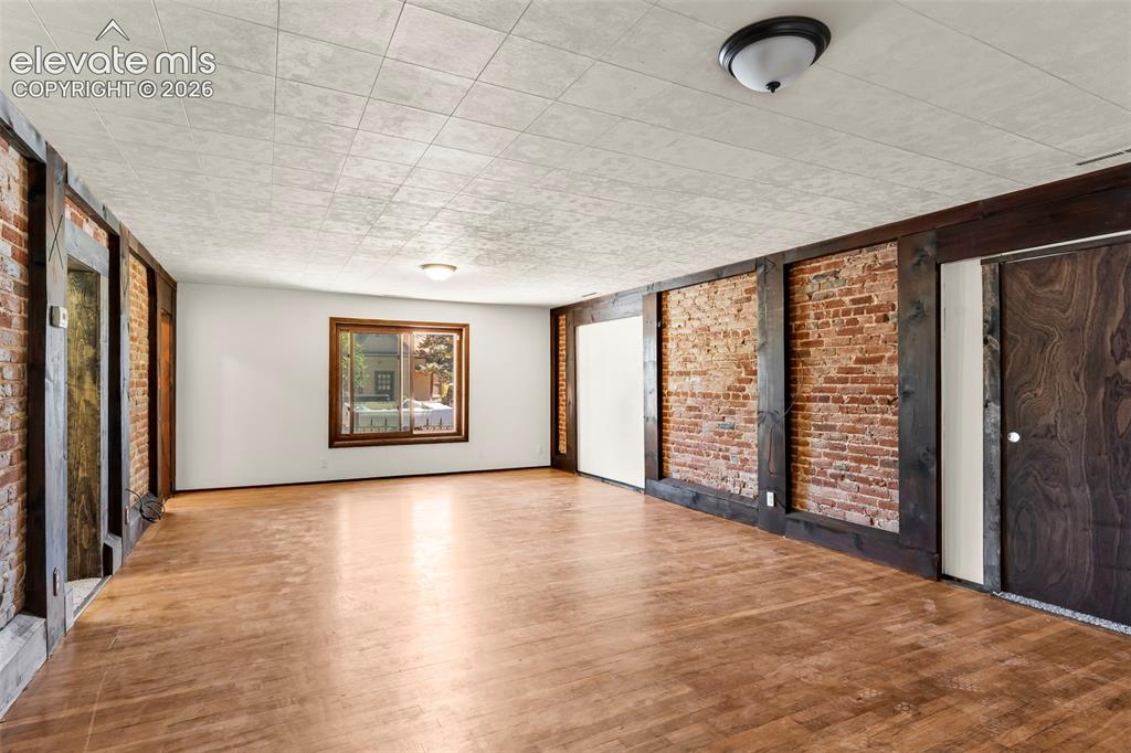 Image 9 of 29: Spacious room featuring exposed brick accent walls with dark wood beams, wo