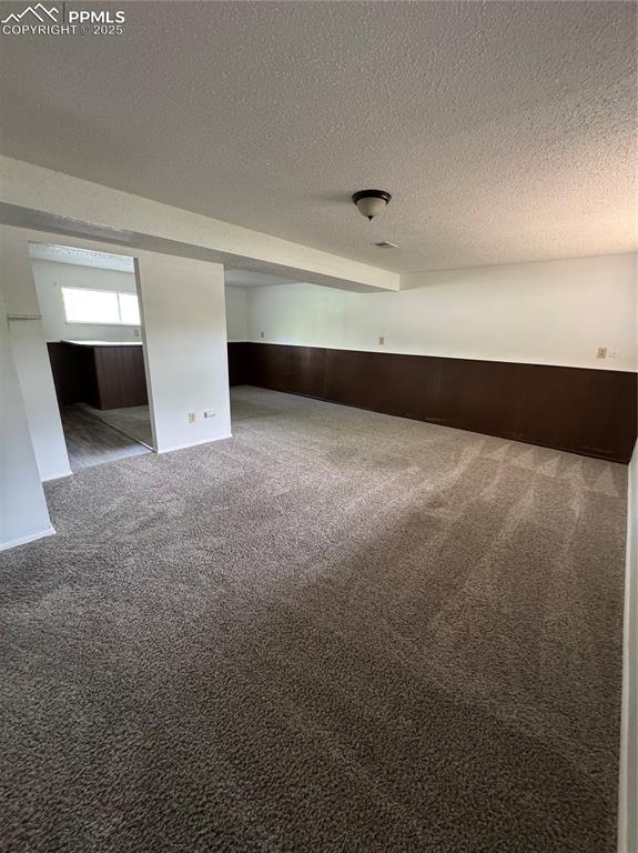 Image 12 of 13: Unfurnished room featuring carpet, a wainscoted wall, and a textured ceilin
