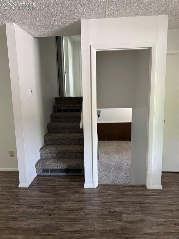 Image 6 of 13: Stairs with a textured ceiling, wood finished floors, and baseboards