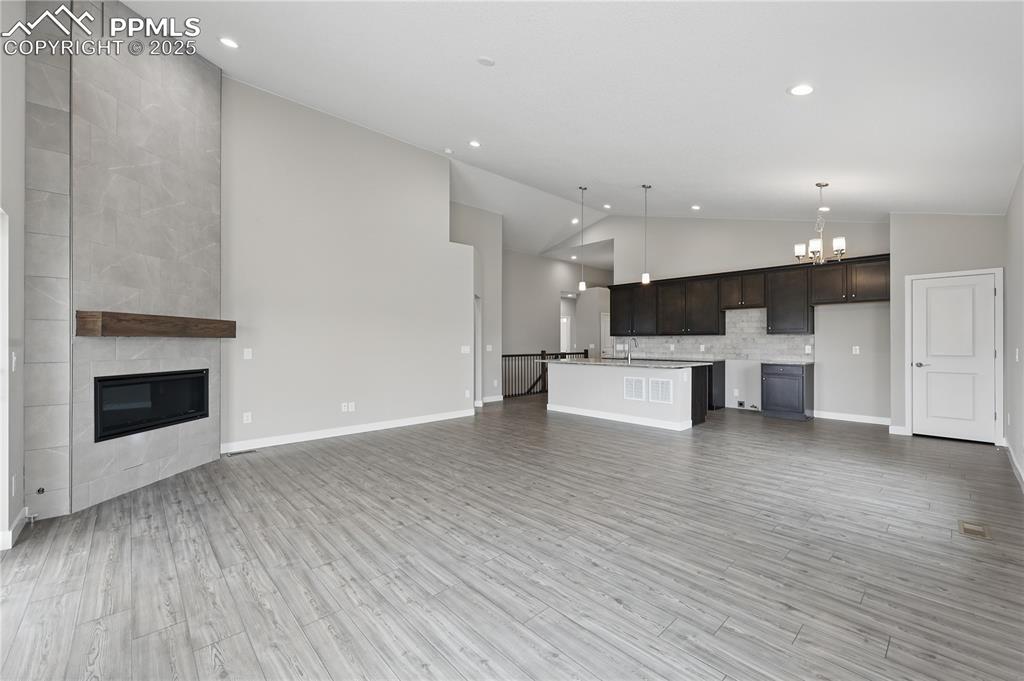 Image 11 of 25: Unfurnished living room with a tiled fireplace, high vaulted ceiling, and r