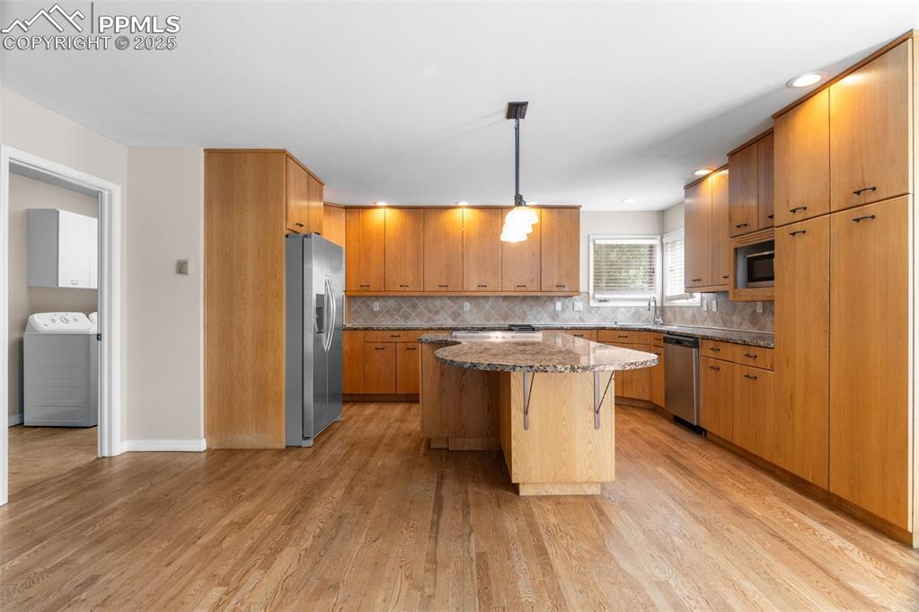 Image 13 of 35: Kitchen with dark stone countertops, pendant lighting, light wood-style flo