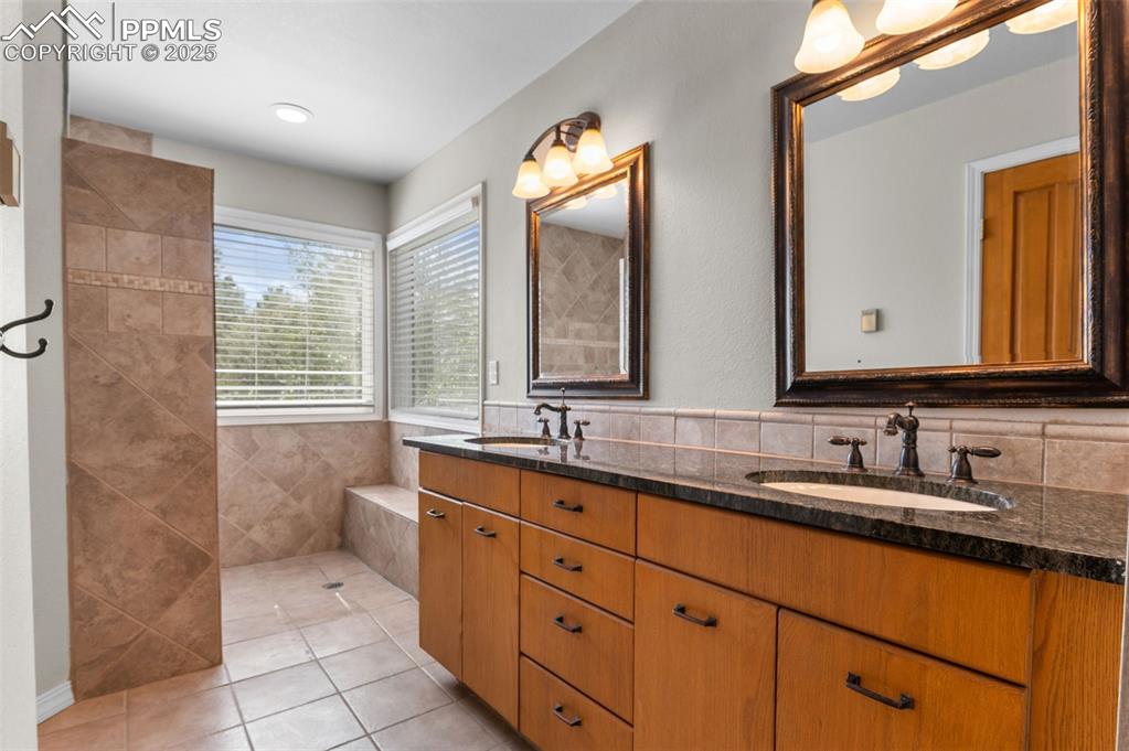 Image 19 of 35: Bathroom with light tile patterned floors, double vanity, tile walls, and a