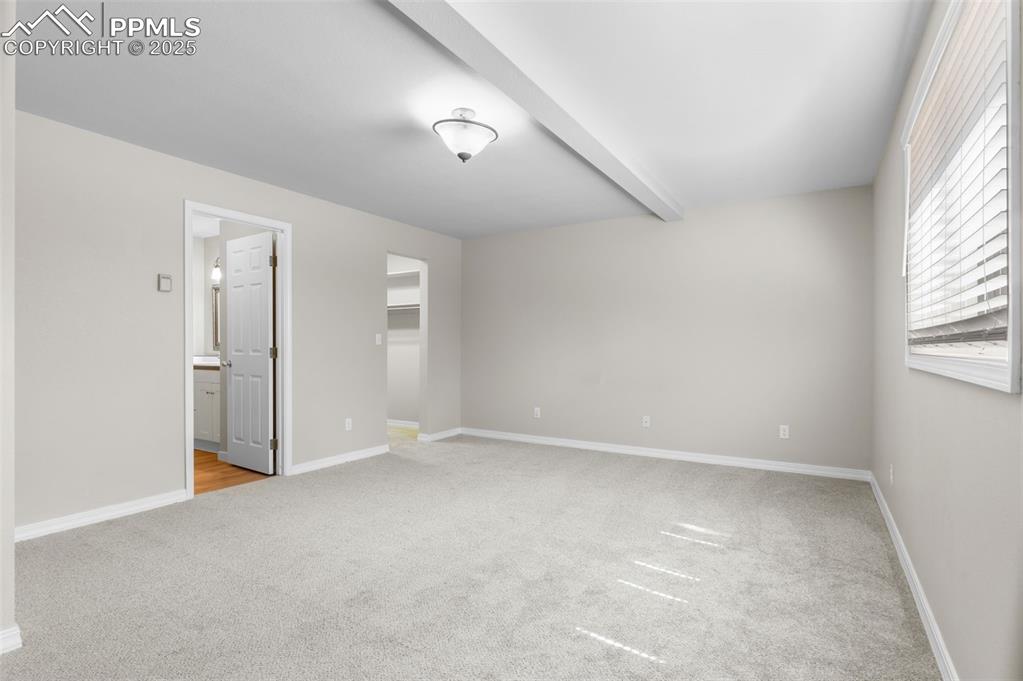 Image 25 of 35: Unfurnished bedroom featuring a spacious closet, light carpet, and beamed c