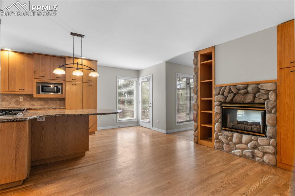 Image 9 of 35: Kitchen with a stone fireplace, dark stone counters, tasteful backsplash, a