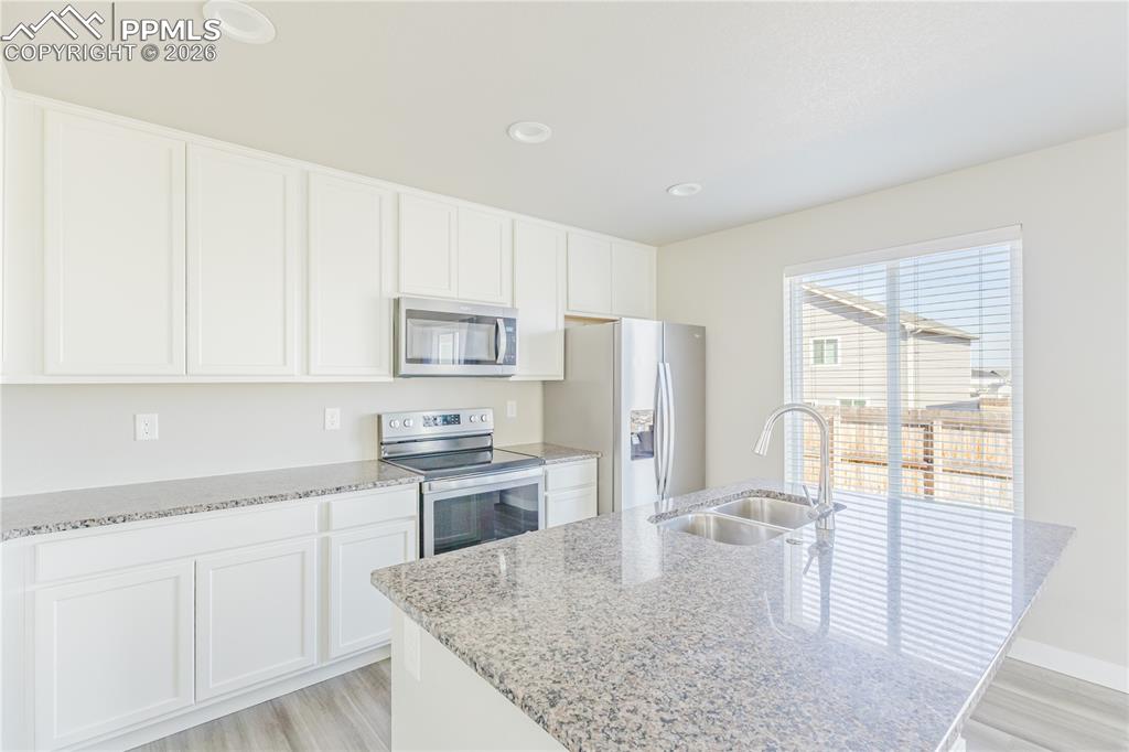 Image 5 of 46: Kitchen with stainless steel appliances, white cabinetry, light stone count