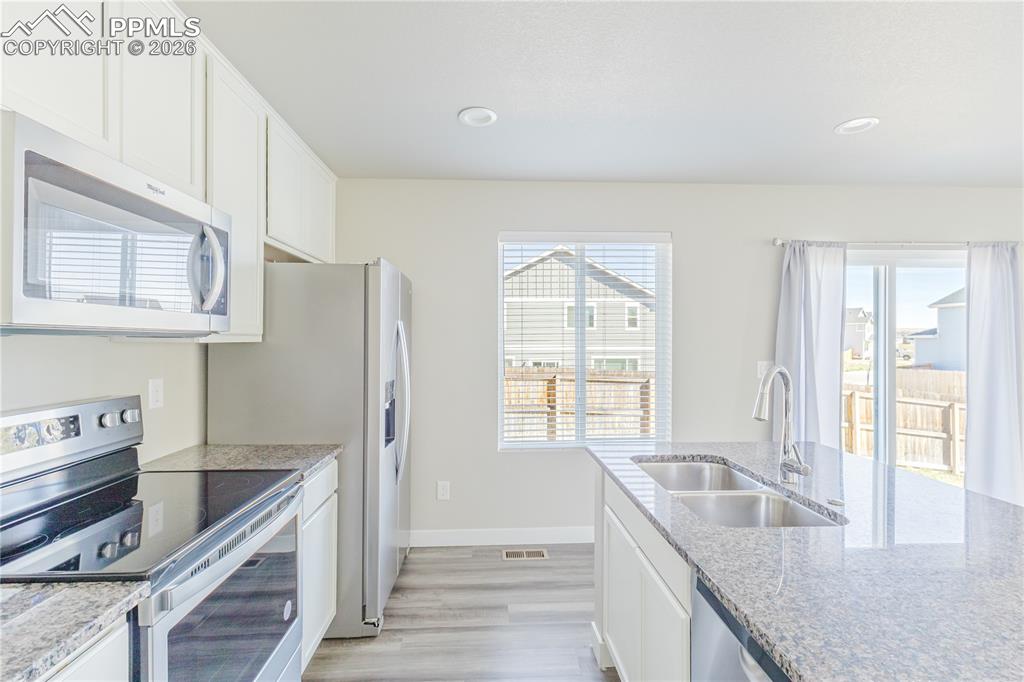 Image 6 of 46: Kitchen featuring stainless steel appliances, white cabinetry, light wood-t