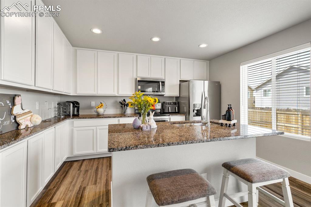 Image 9 of 46: Kitchen featuring white cabinetry, dark wood-type flooring, dark stone coun