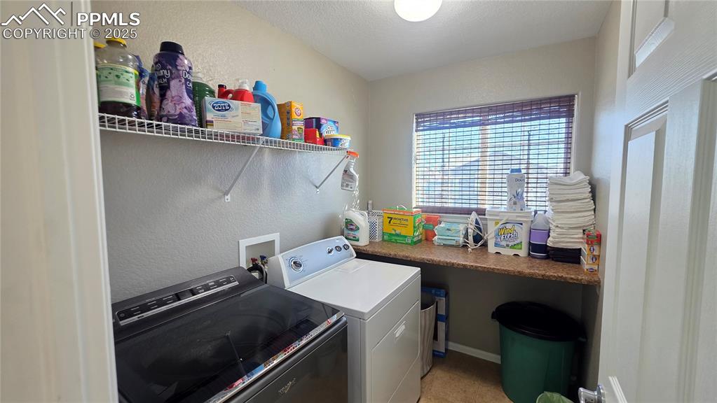 Image 29 of 34: Washroom with a textured wall, washing machine and clothes dryer, and a tex