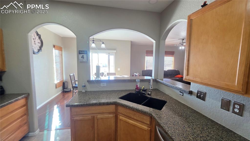 Image 9 of 34: Kitchen featuring arched walkways, dark stone counters, brown cabinetry, an