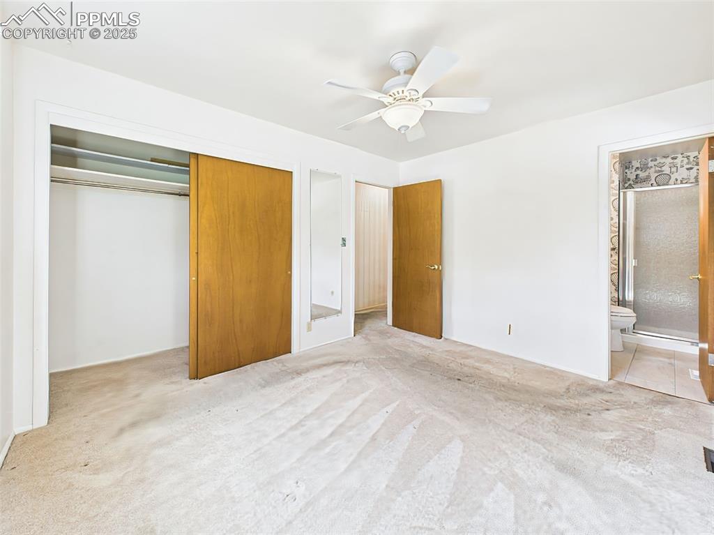 Image 19 of 40: The carpeted primary bedroom offers a very large, deep closet, ceiling fan,