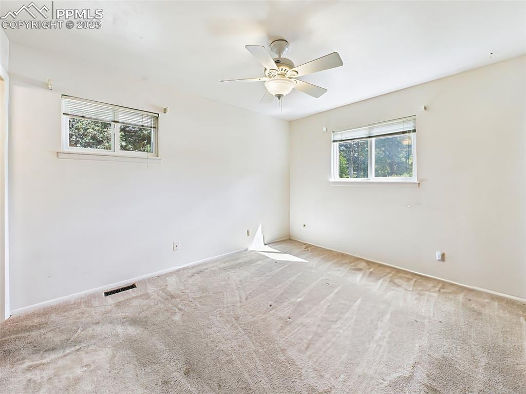 Image 21 of 40: Carpeted primary bedroom with 2 windows and ceiling fan!