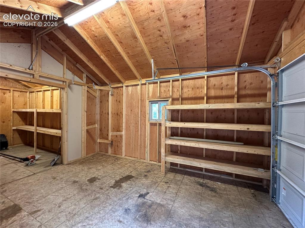 Image 46 of 50: Storage shed with overhead door and shelves.