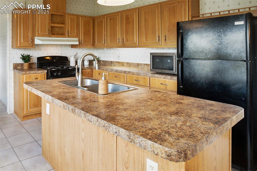 Image 15 of 49: Kitchen with black appliances, wallpapered walls, a sink, under cabinet ran
