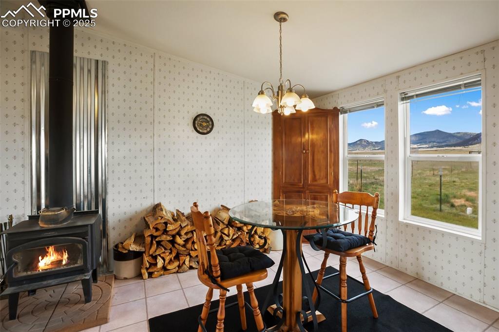 Image 16 of 49: Dining space with a wood stove, wallpapered walls, light tile patterned flo