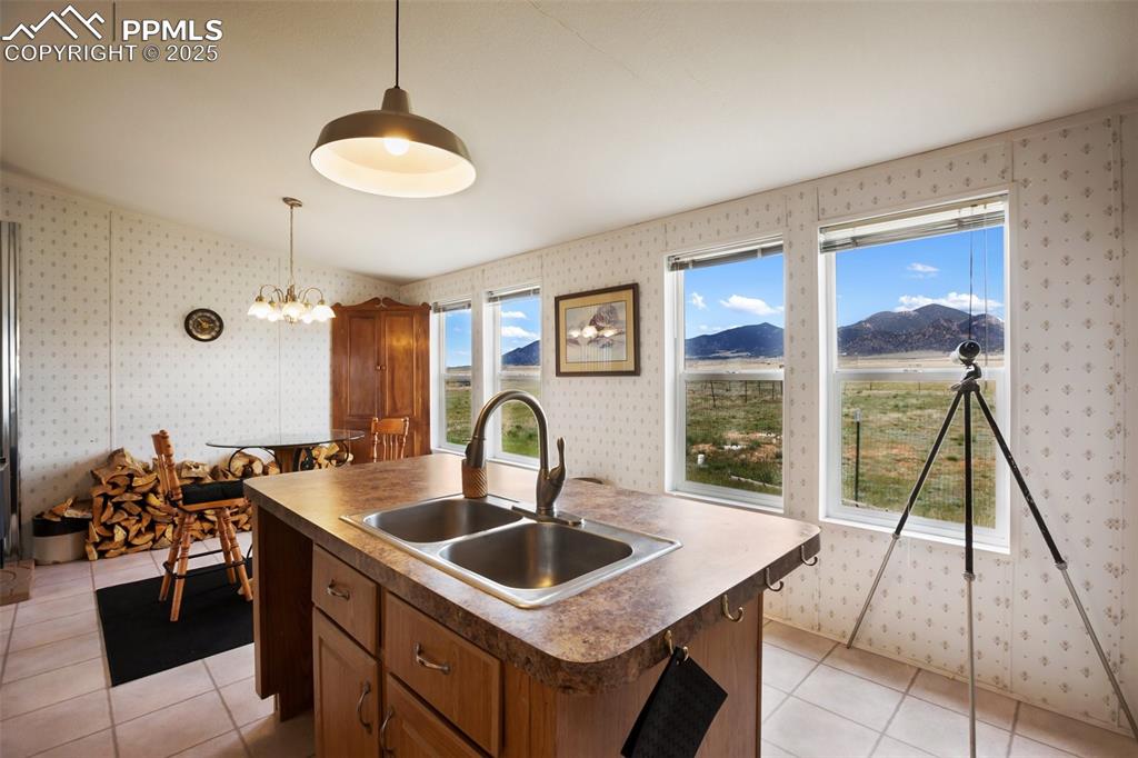 Image 21 of 49: Kitchen with a sink, wallpapered walls, brown cabinets, light tile patterne