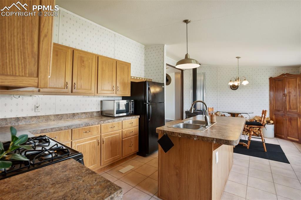 Image 22 of 49: Kitchen with wallpapered walls, black appliances, a sink, light tile patter