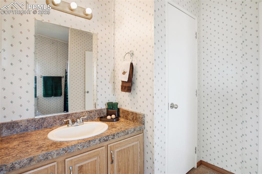 Image 28 of 49: Bathroom featuring wallpapered walls and vanity