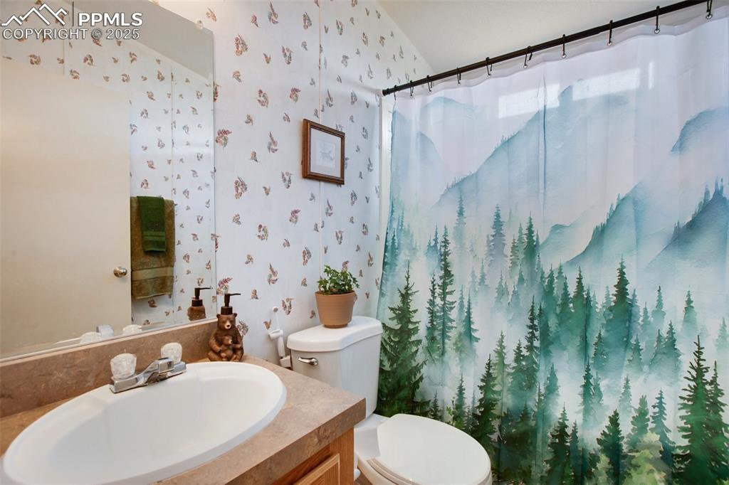 Image 30 of 49: Full bathroom featuring wallpapered walls, vanity, toilet, and a shower wit