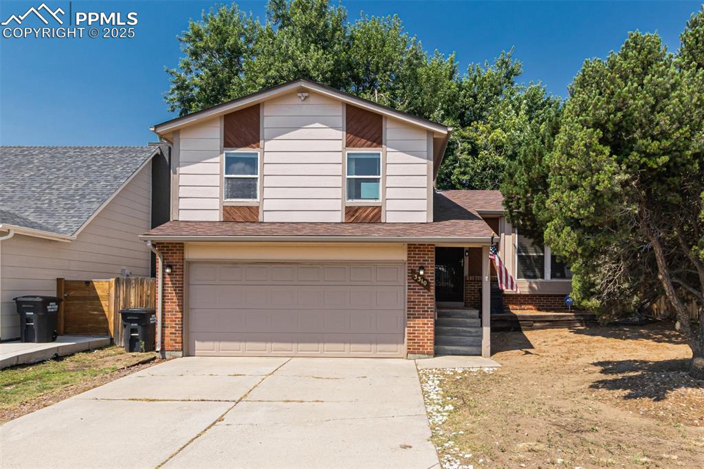 Image 1 of 43: Tri-level home with an attached garage, a shingled roof, driveway, and bric