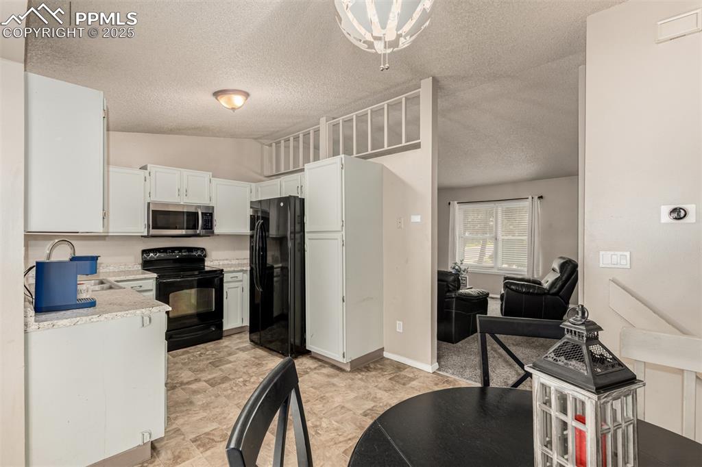 Image 11 of 43: Kitchen with black appliances, lofted ceiling, a textured ceiling, and whit