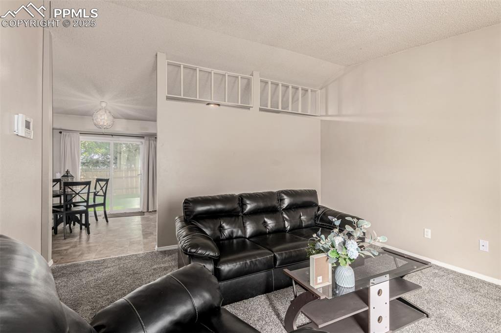 Image 5 of 43: Carpeted living area featuring lofted ceiling and a textured ceiling