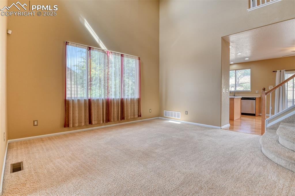 Image 12 of 49: Unfurnished room with a towering ceiling, carpet, and stairway