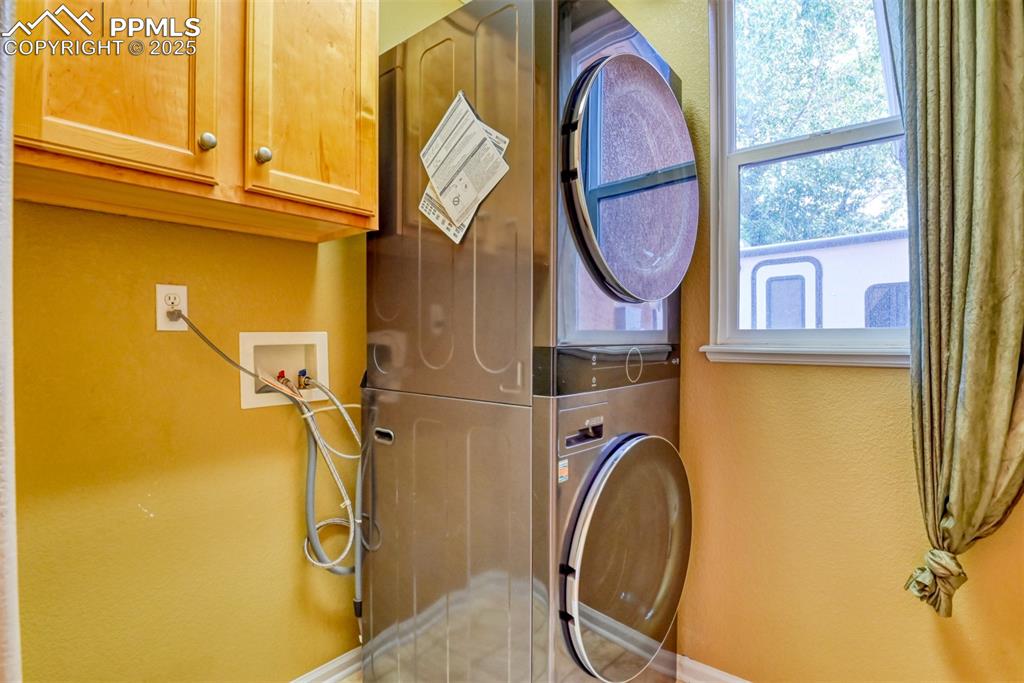 Image 24 of 49: Washroom featuring a textured wall, cabinet space, and stacked washer / dry