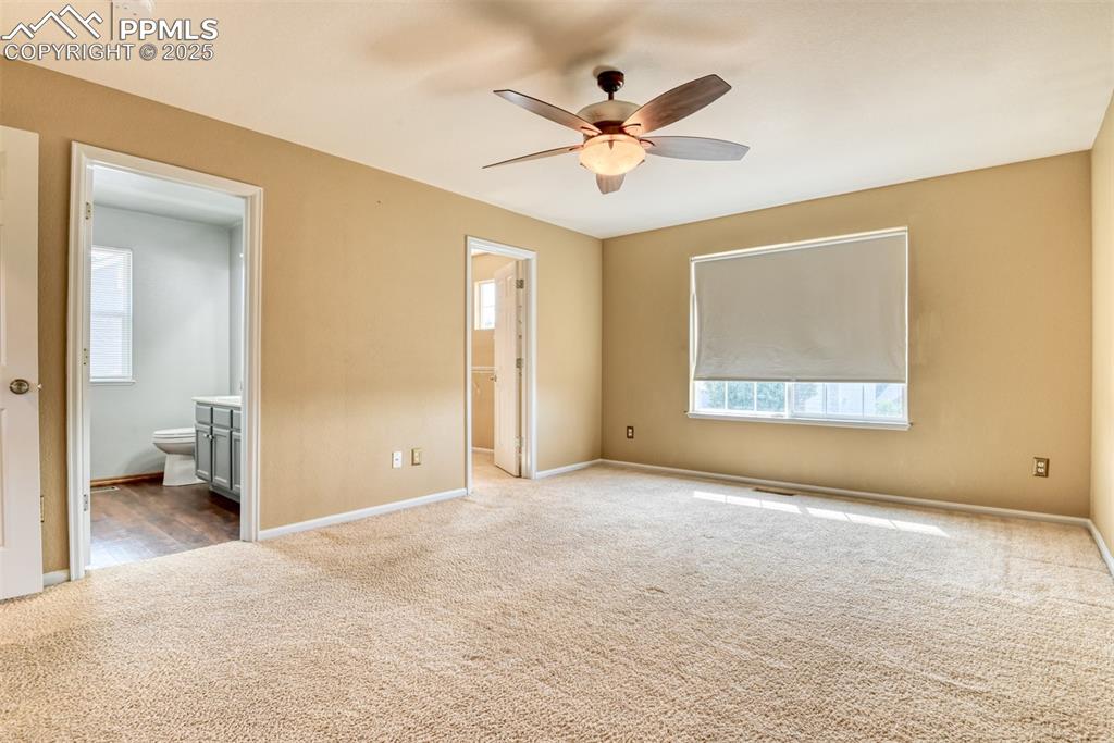Image 26 of 49: Unfurnished bedroom with dark carpet, ensuite bathroom, and a ceiling fan