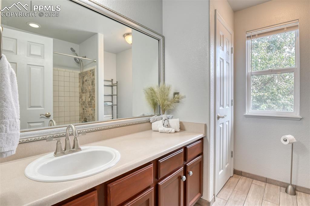 Image 37 of 49: Full bath featuring vanity, a tile shower, a textured wall, and wood tiled