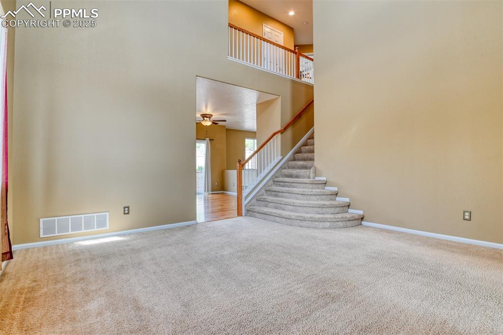 Image 7 of 49: Unfurnished living room with a towering ceiling, carpet, and stairs