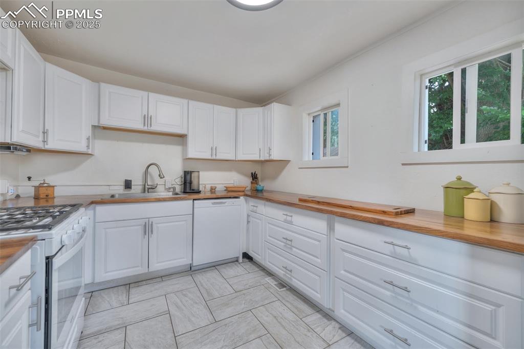 Image 16 of 38: Bright white Shaker cabinets, stainless appliances, and butcher block count