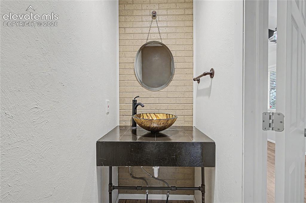 Image 15 of 46: Powder room featuring a vessel sink, dark countertop, and decorative brick